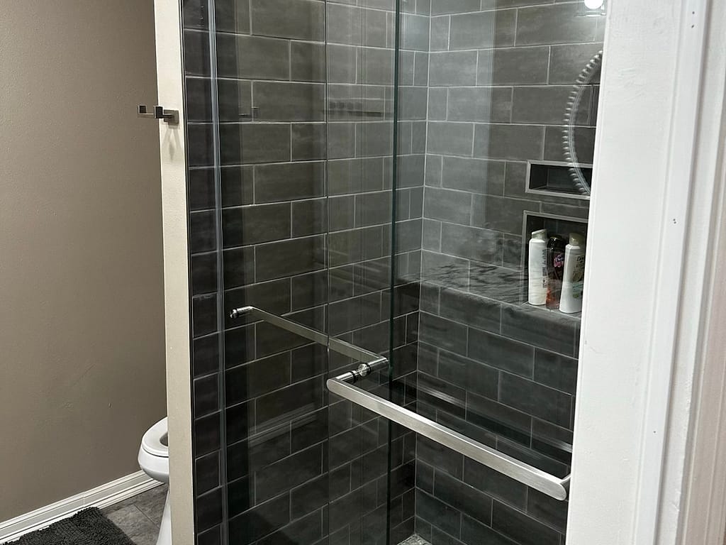 Bathroom with shower that has sliding glass doors and grey tile after remodel